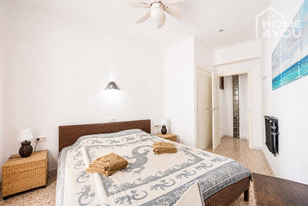 Helles Schlafzimmer mit Rattanbett, Deckenventilator und Zugang zu einem Flur.