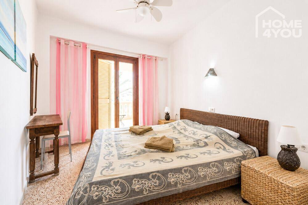 Schlafzimmer mit Rattanbett, Deckenventilator und rosa Vorhängen.