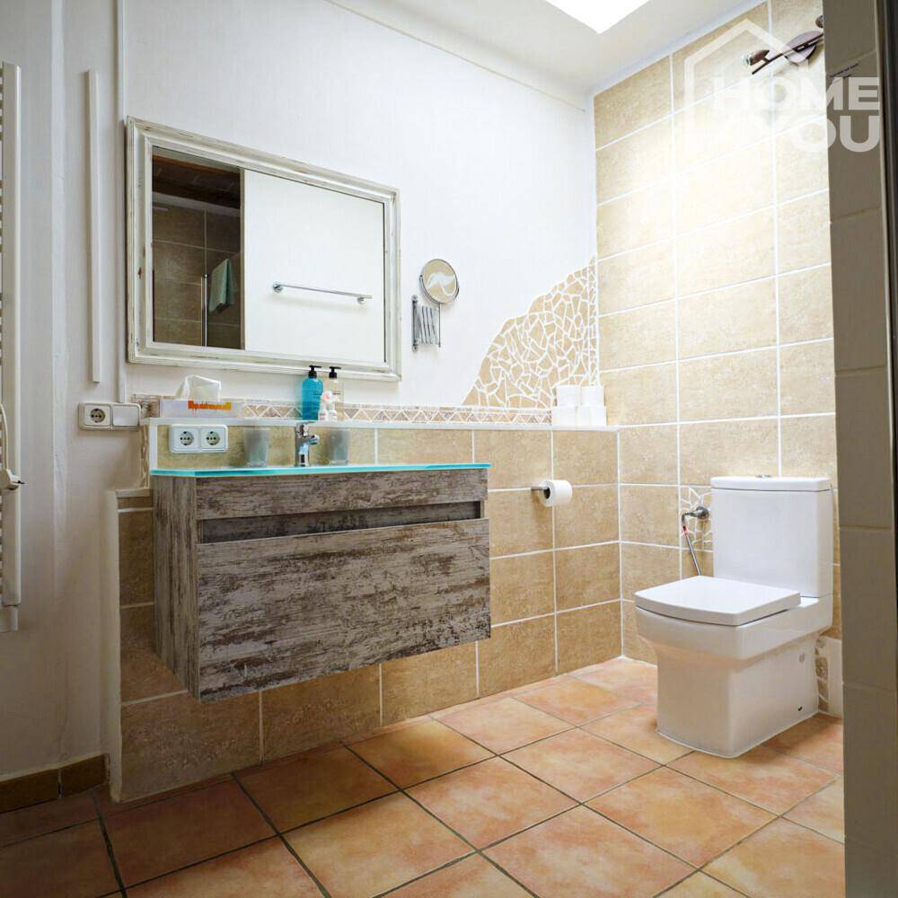 Helles Badezimmer mit schwebendem Waschtisch, Toilette und beigefarbenen Fliesen.