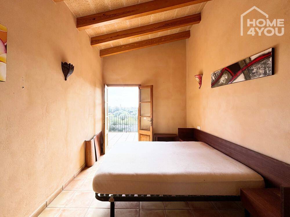 Schlafzimmer mit Holzbalkendecke, Fliesenboden und Zugang zu einem Balkon mit Aussicht.