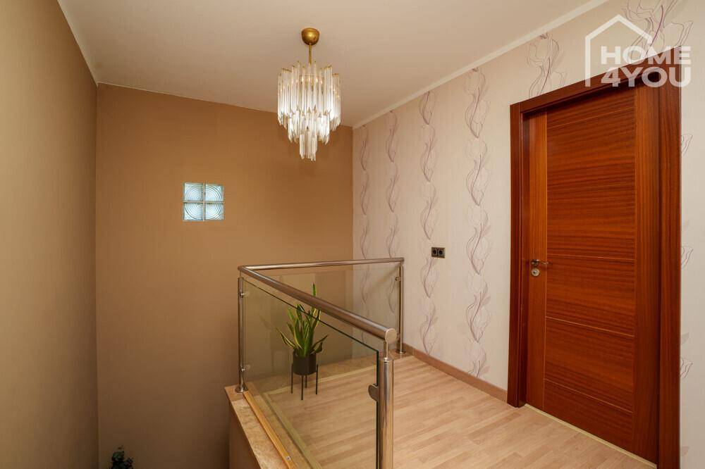 Heller Flur mit moderner Glasbrüstung, elegantem Kronleuchter und dekorativer Tapete.