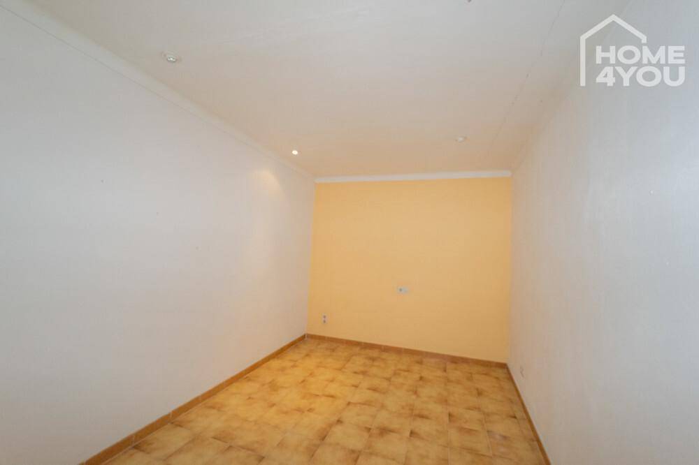 Kleiner, leerer Raum mit Fliesenboden und einer gelben Akzentwand, ideal als Schlafzimmer.