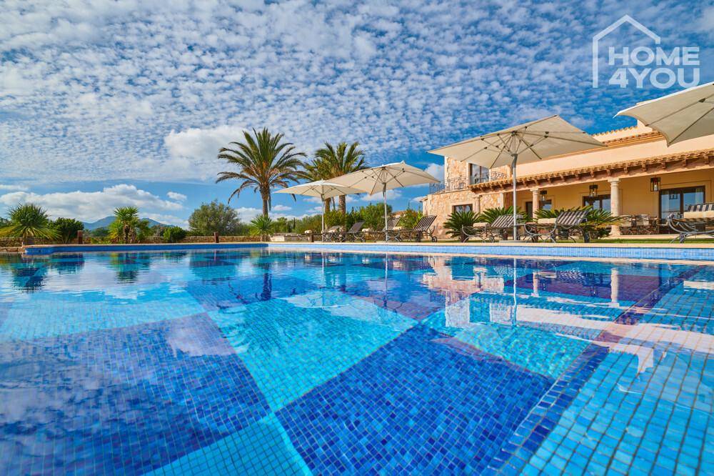 Weitläufiger Poolbereich mit blauen Fliesen und Sonnenschirmen vor der Villa.