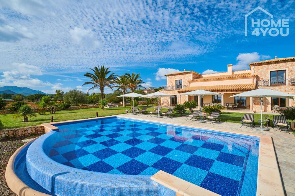Geschwungener Poolbereich mit blauen Fliesen und Liegestühlen vor der mediterranen Villa.