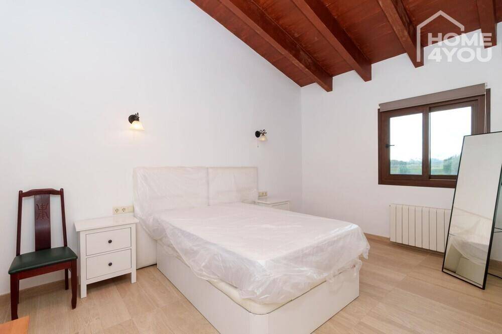 Helles Schlafzimmer mit Holzbalkendecke, einfachem Bett und Nachttischen, bereit zur Einrichtung.
