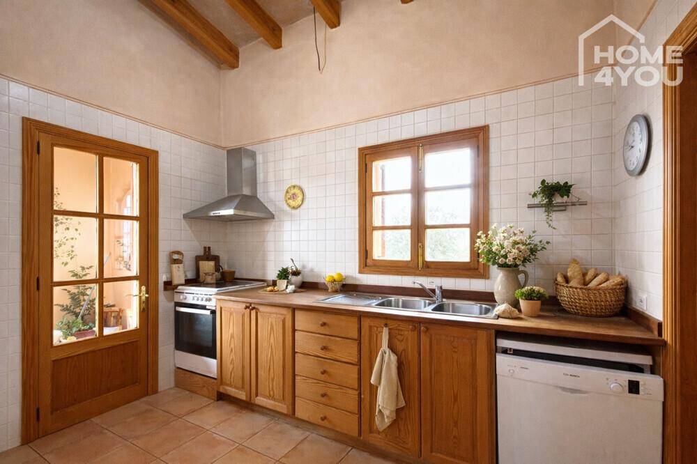 Traditionelle Küche mit Holzschränken, Fliesenboden und Blick nach draußen durch das Fenster.