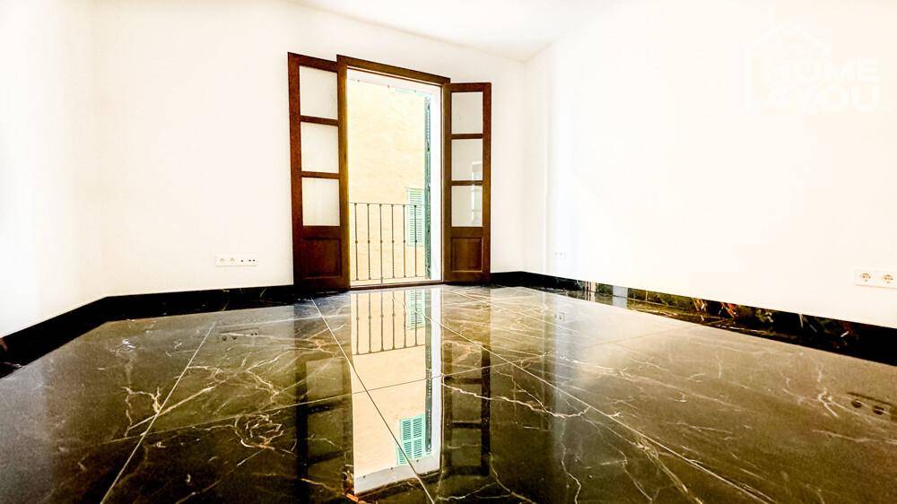 Leeres Schlafzimmer mit dunklem Marmorboden und Zugang zu einem französischen Balkon.