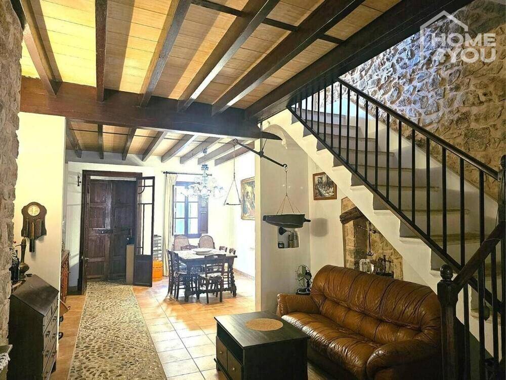 Gemütlicher Wohnbereich mit Steinfliesen, Holzbalkendecke und einer eleganten Treppe.