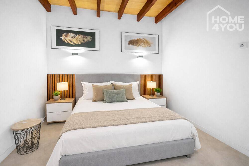 Gemütliches Schlafzimmer mit Doppelbett, Nachttischen und dekorativer Holzwandverkleidung unter Holzbalken.