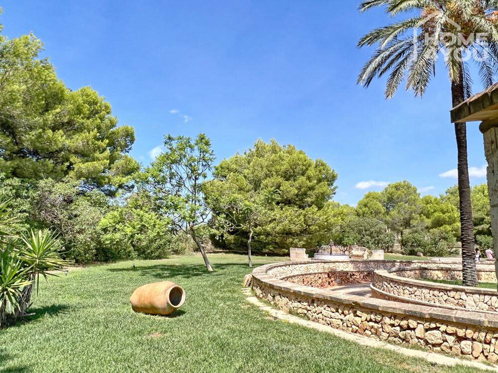 Gepflegter Gartenbereich mit traditioneller Steinmauer, einer antiken Amphore und üppiger Vegetation.