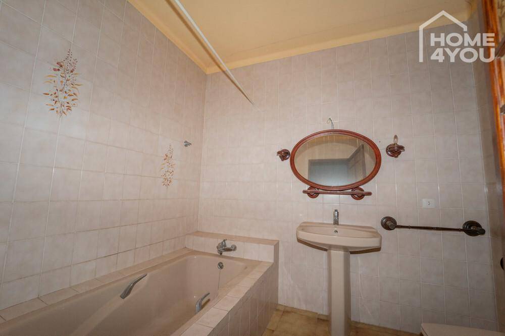 Gefliestes Badezimmer mit Badewanne, Standwaschbecken und ovalem Spiegel.
