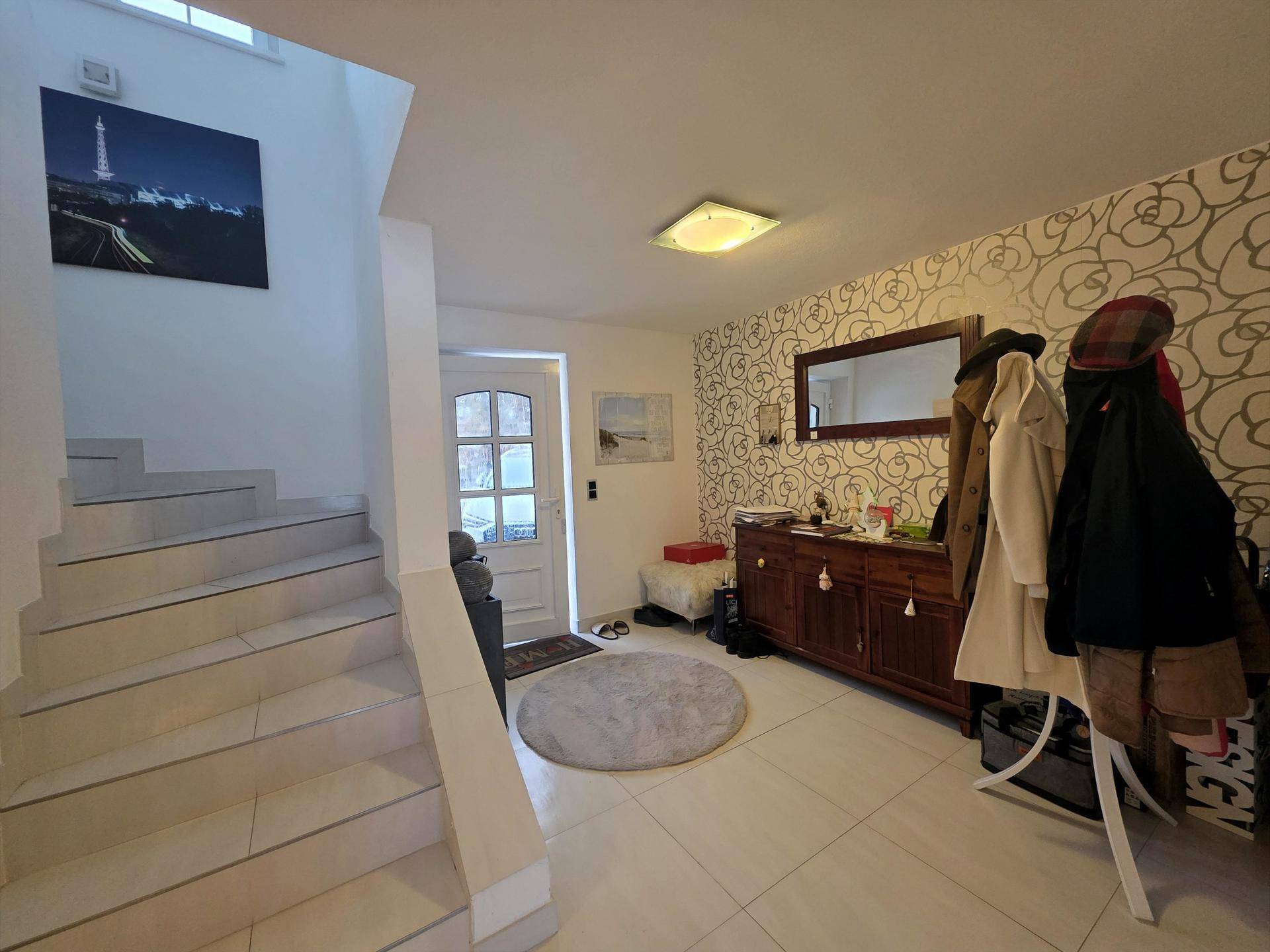 Geräumiger Eingangsbereich mit Treppe, Fliesenboden und einer stilvollen Garderobe.