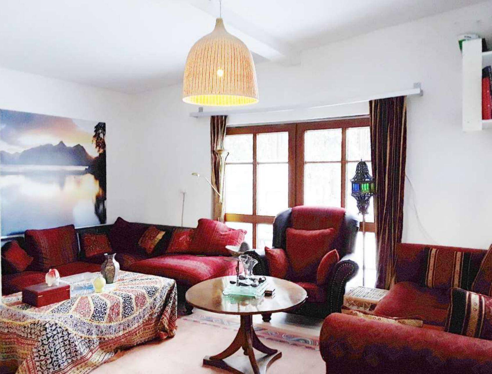 Gemütliches Wohnzimmer mit roten Sofas, Holztisch und einem großen Fenster mit Blick nach draußen.