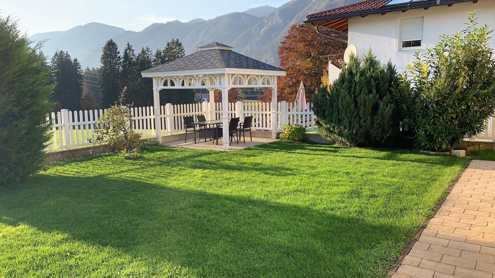 Gepflegter Garten mit Rasenfläche, weißem Pavillon und malerischem Bergblick im Hintergrund.