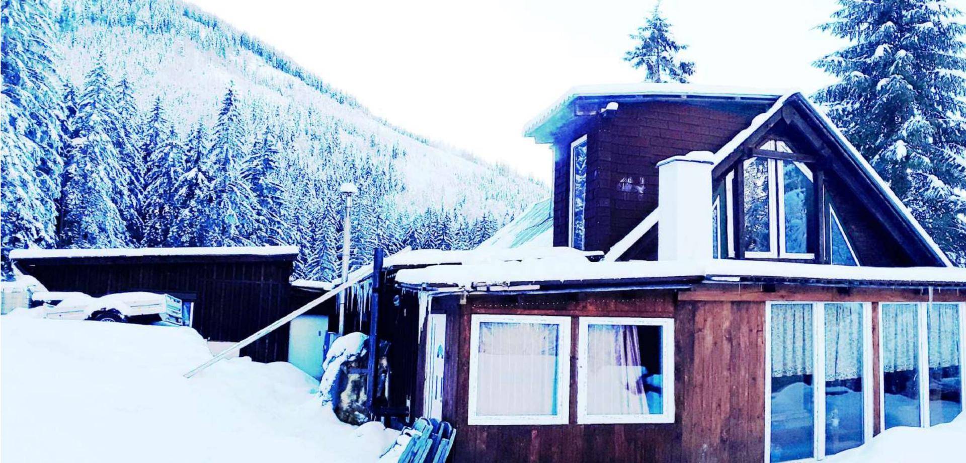 Rustikales Holzhaus mit großen Fenstern und schneebedecktem Dach in alpiner Umgebung.