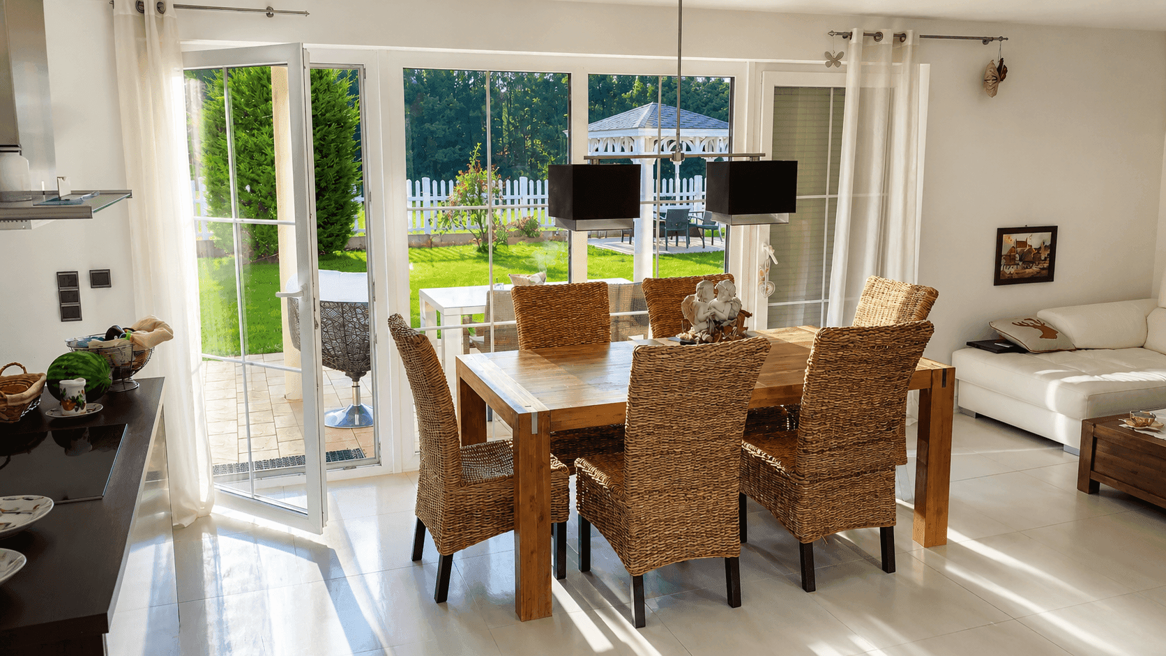 Essbereich mit Holztisch und Korbstühlen, großen Fenstern und Blick in den Garten.