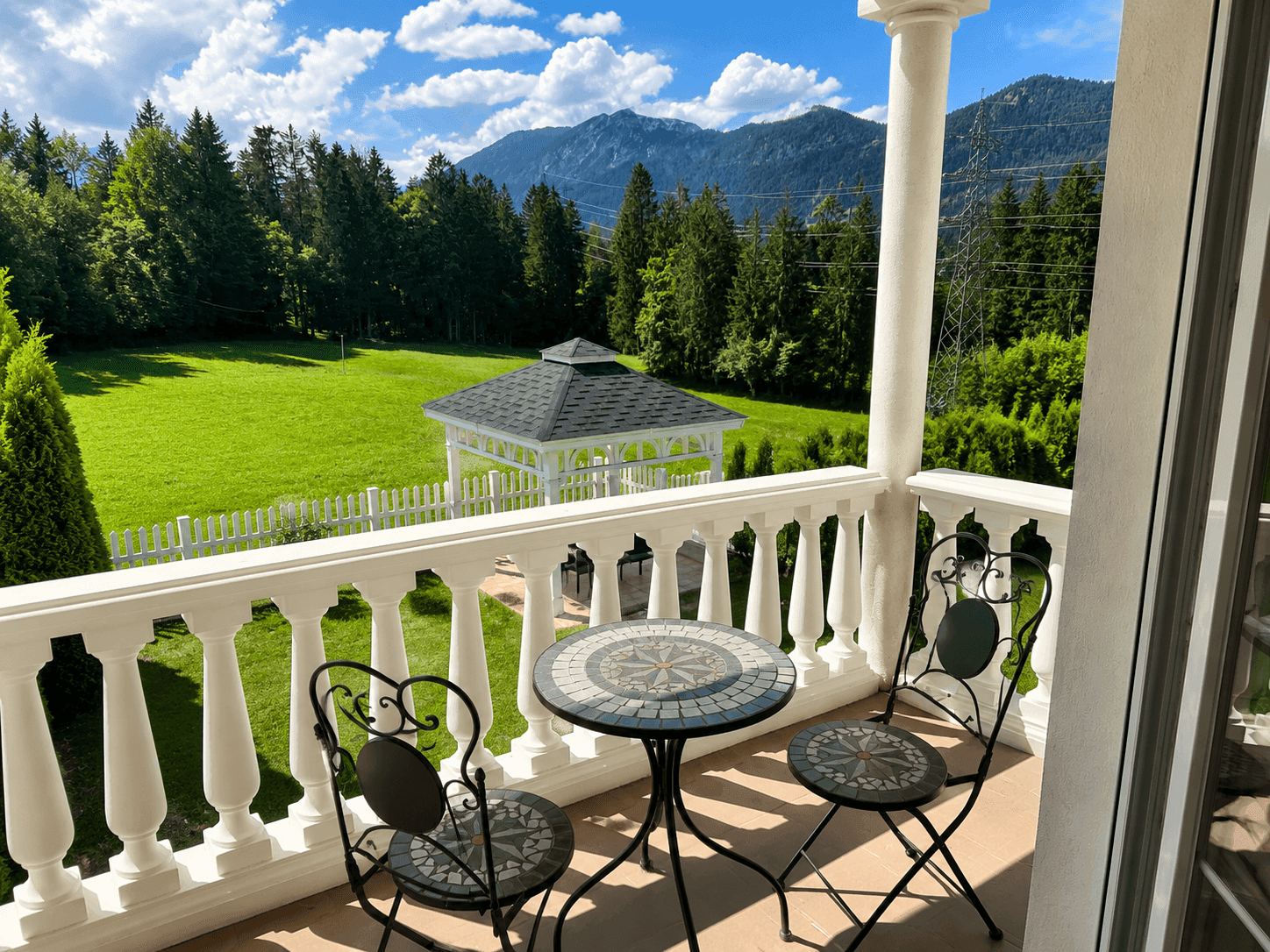 Balkon mit schmiedeeisernen Möbeln und weitem Blick auf die Berge und den Garten.