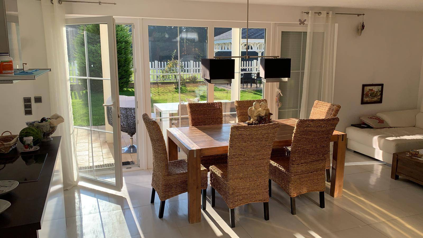 Heller Essbereich mit Holztisch, Korbstühlen und direktem Zugang zum Garten durch große Glastüren.