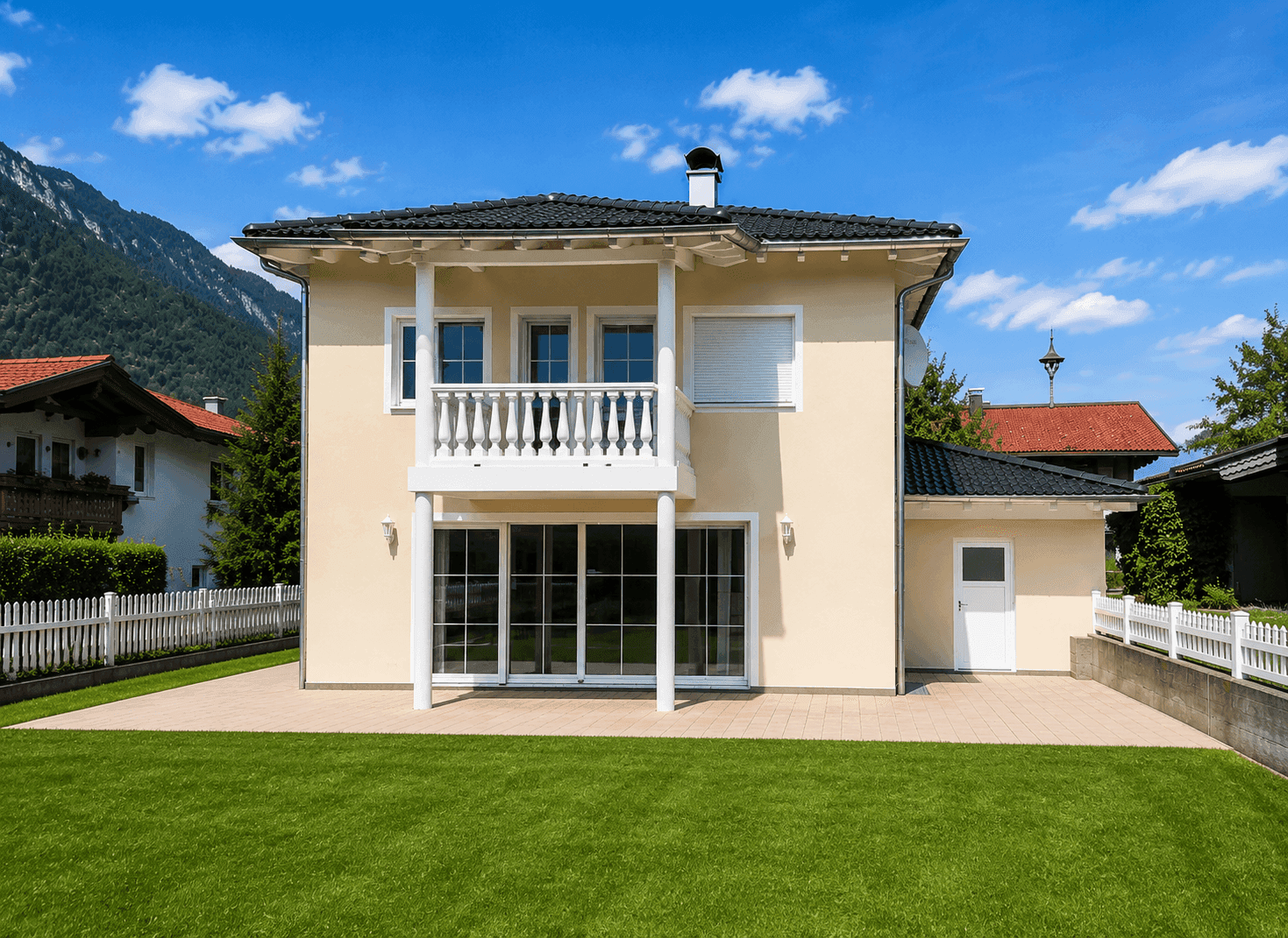 Rückseite des Hauses mit Balkon, großen Fenstern und gepflegtem Rasen.