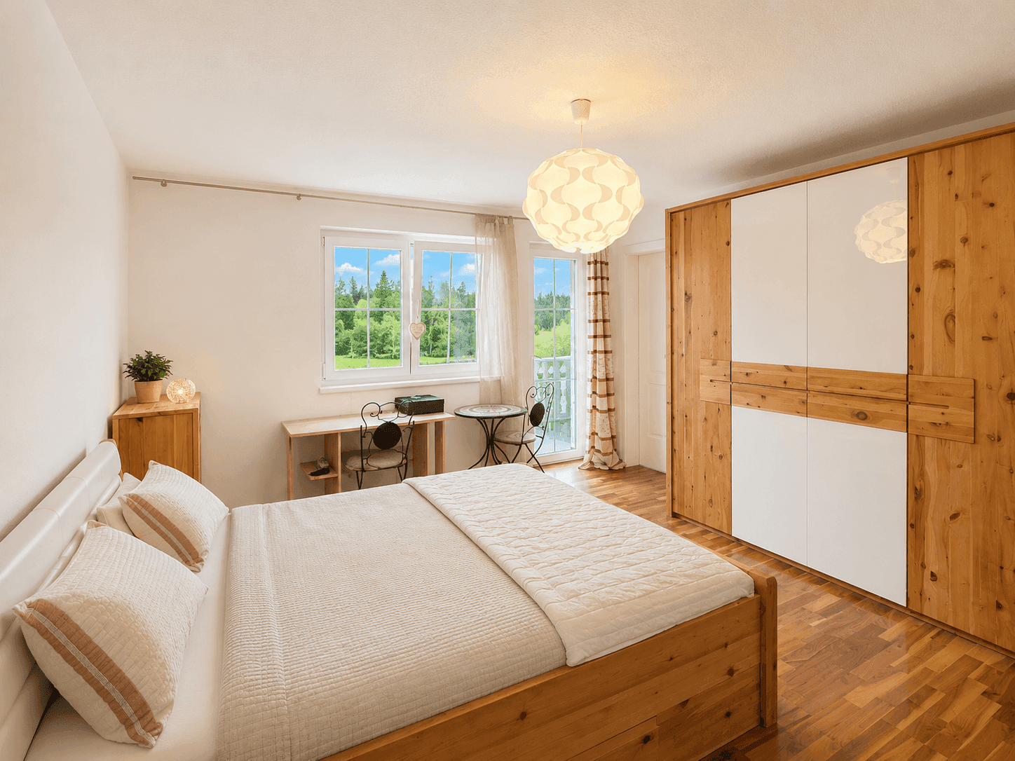 Helles Schlafzimmer mit Holzboden, Holzkleiderschrank und Zugang zum Balkon.