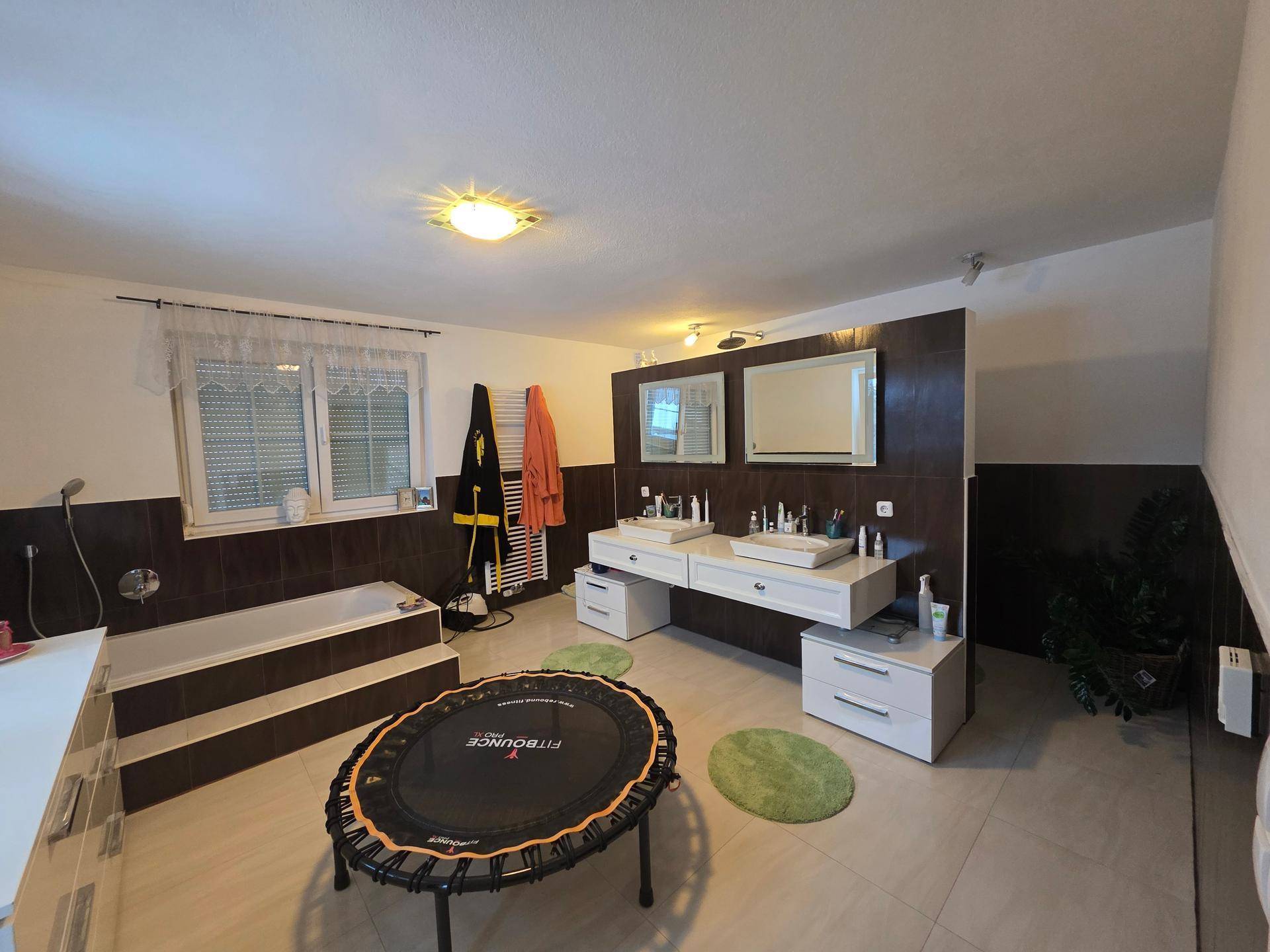 Geräumiges Badezimmer mit Doppelwaschbecken, Badewanne, Fenster und Fliesenboden.