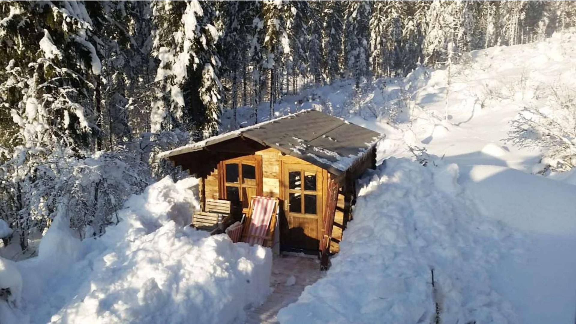 Kleine Holzhütte umgeben von tiefem Schnee in einer winterlichen Waldlandschaft.