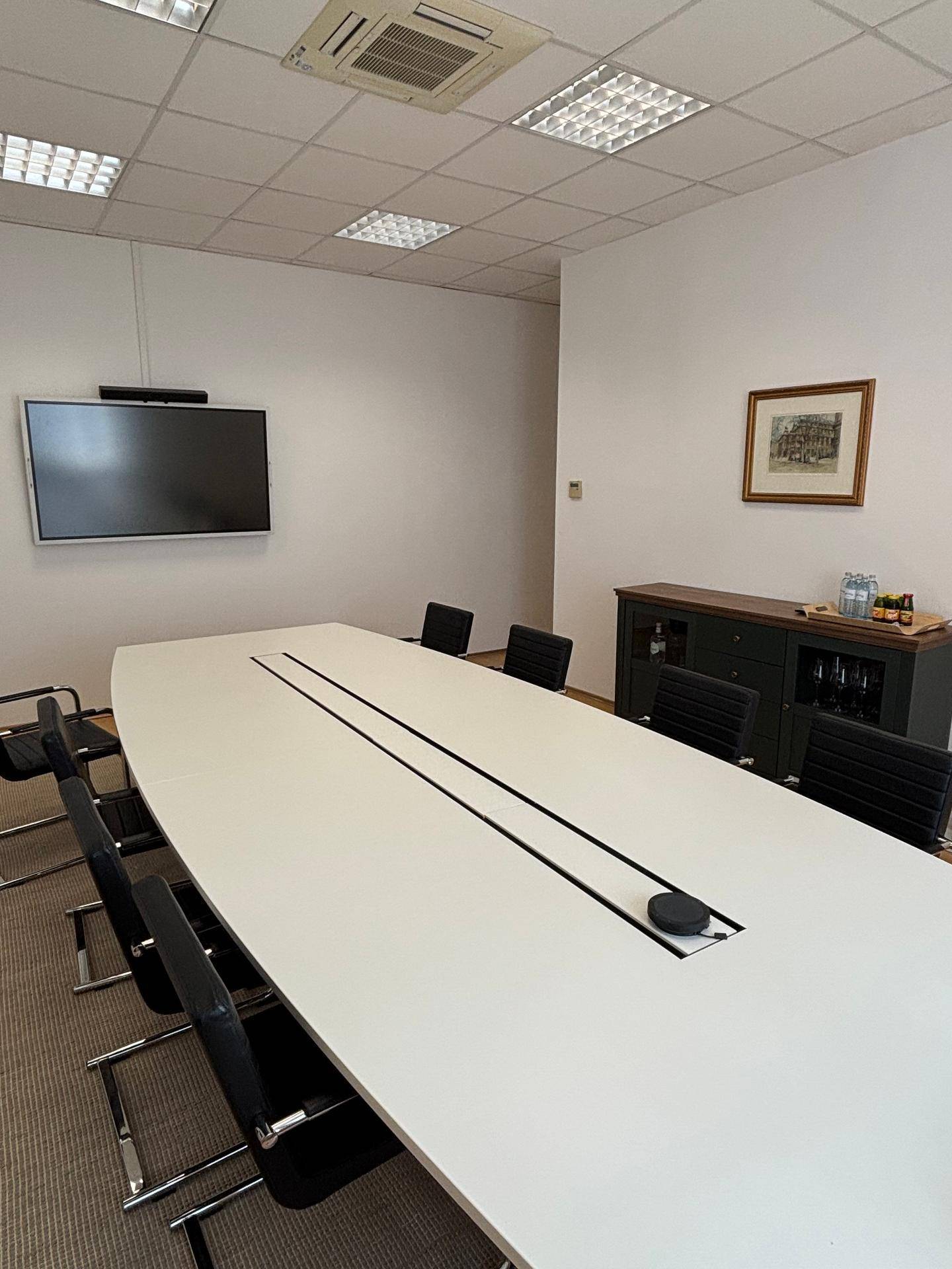 Konferenzraum mit großem Tisch, Wandfernseher, Sideboard und Klimaanlage an der Decke.