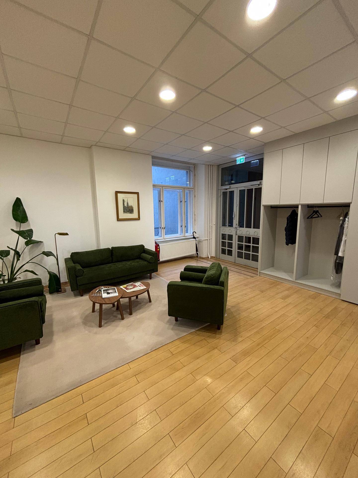 Heller Empfangsbereich mit grünen Sitzmöbeln, Garderobe, großem Fenster und natürlichem Lichteinfall.