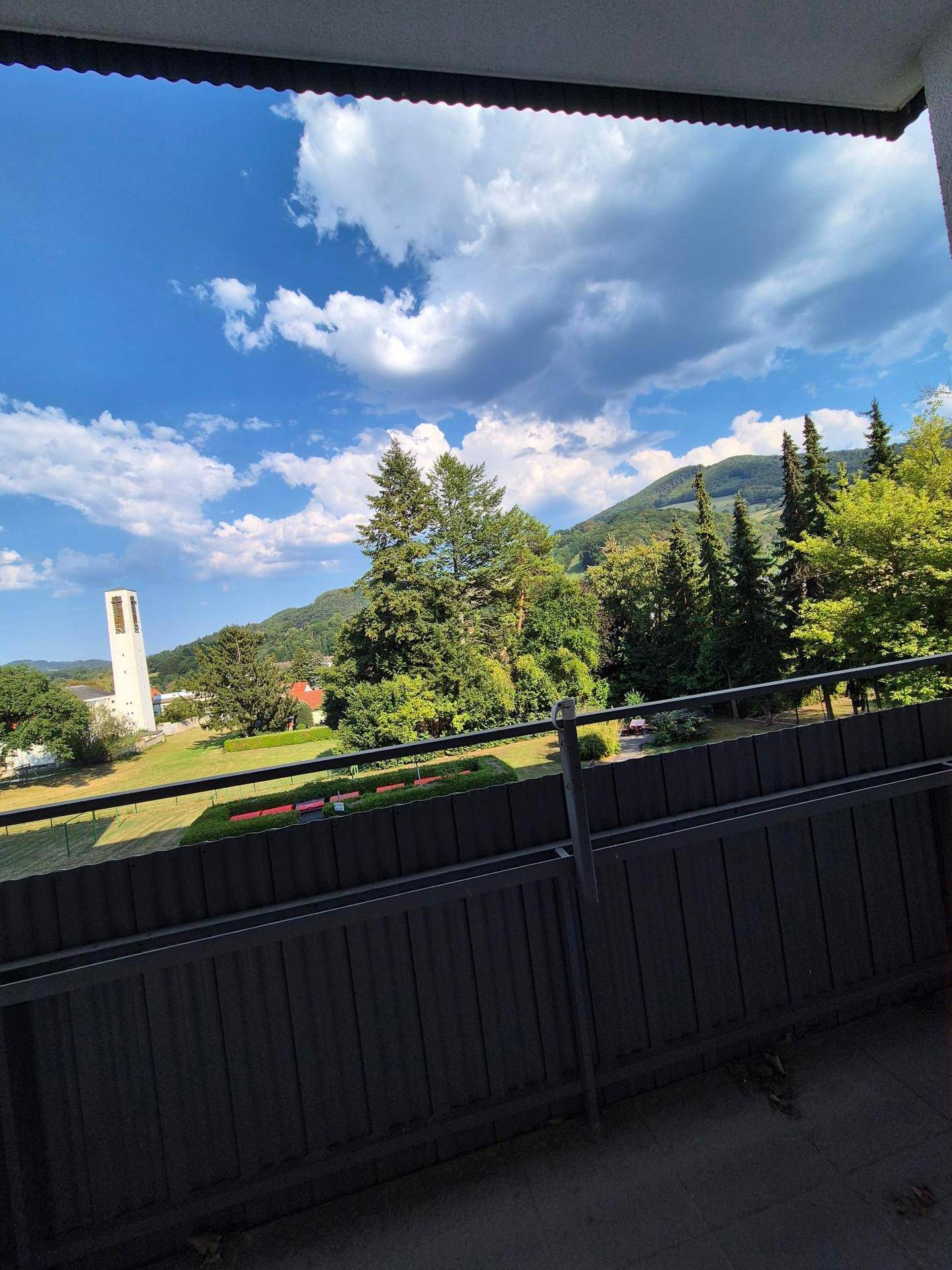Panoramablick vom Balkon auf grüne Hügel, Bäume und einen markanten Turm unter blauem Himmel.