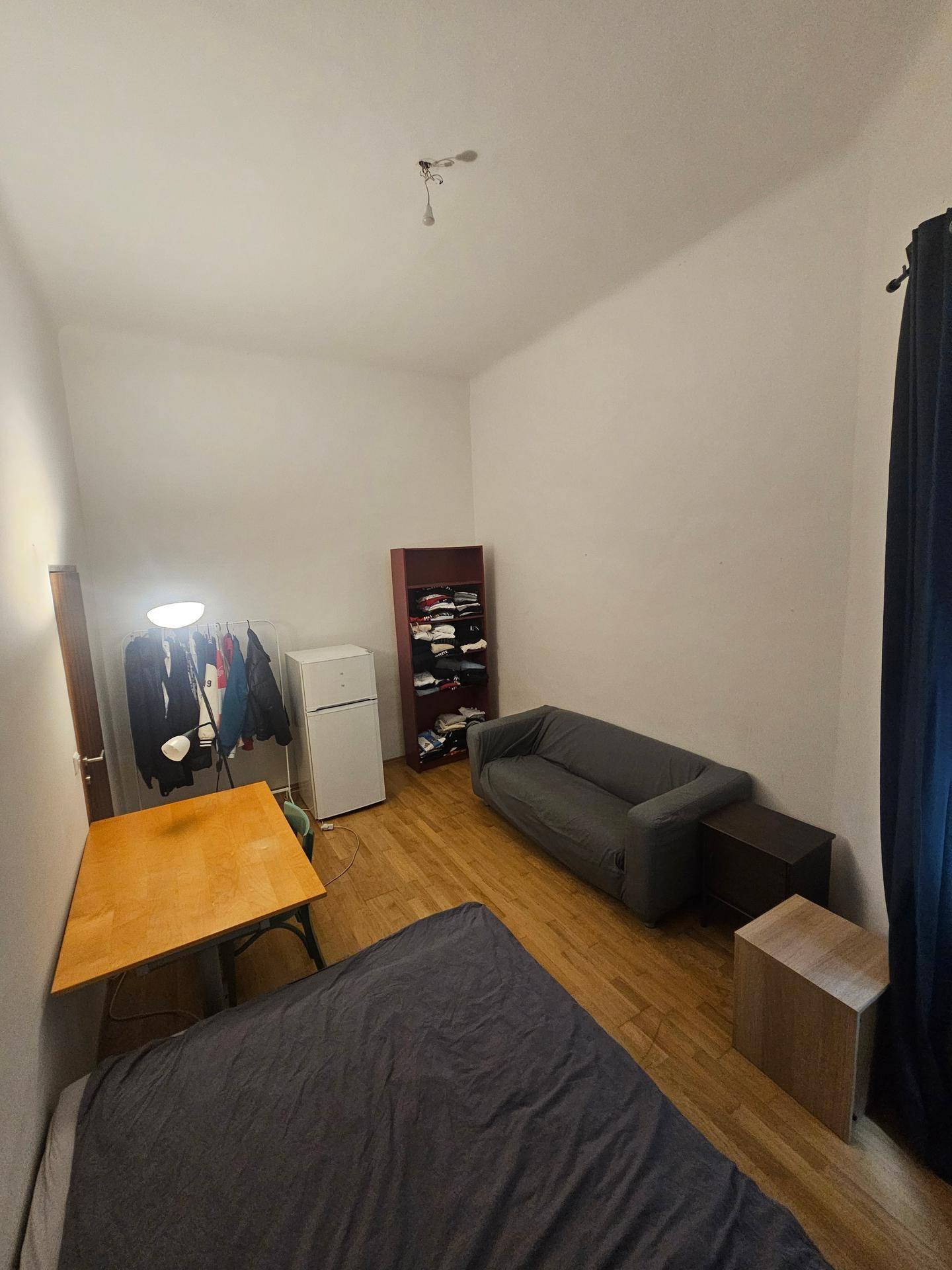 Geräumiges Schlafzimmer mit Sofa, Kühlschrank und Kleiderstange, bietet vielseitige Nutzungsmöglichkeiten.