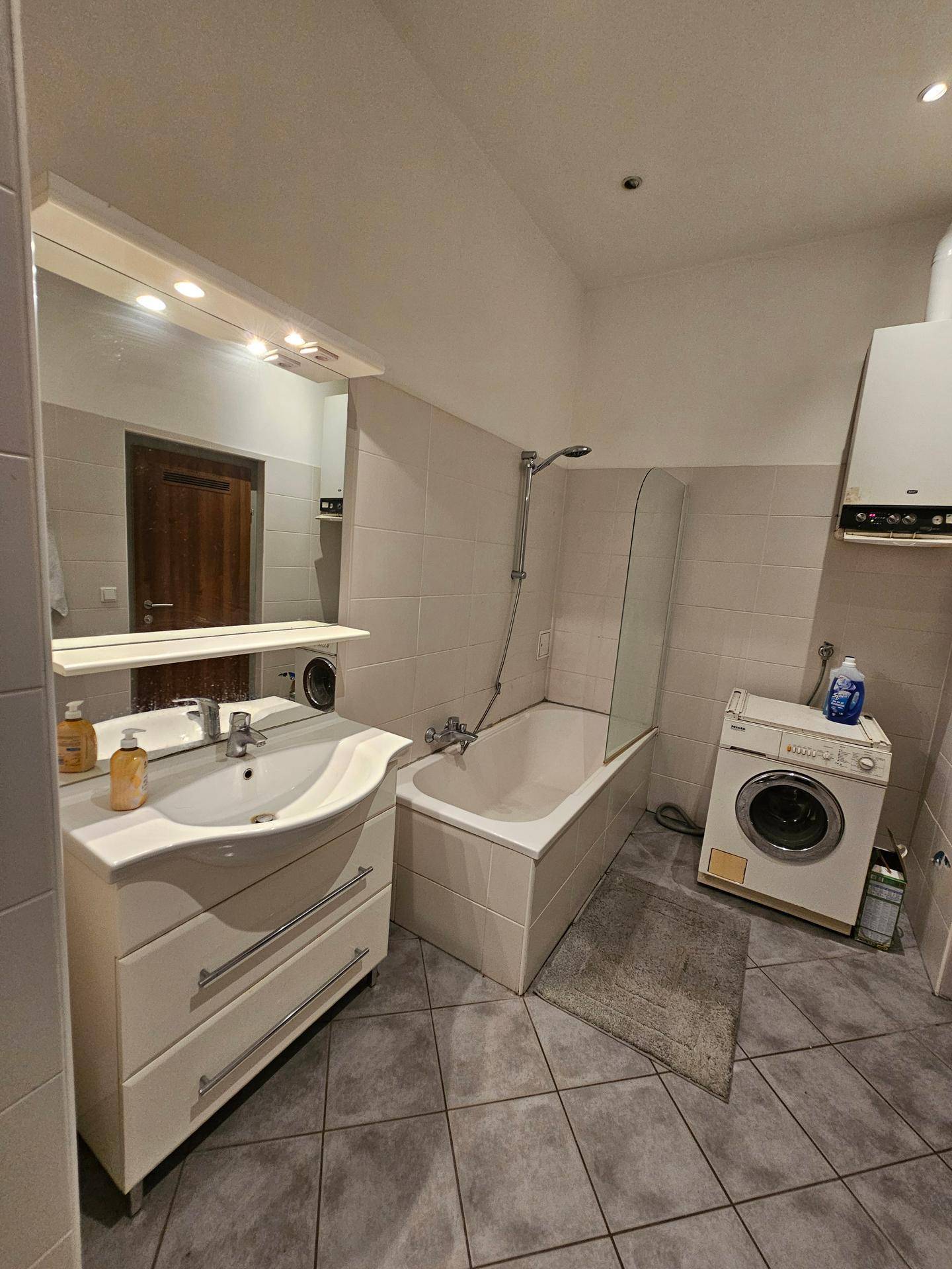 Badezimmer mit Badewanne, Waschbecken und Waschmaschine, hell gefliest und funktional.