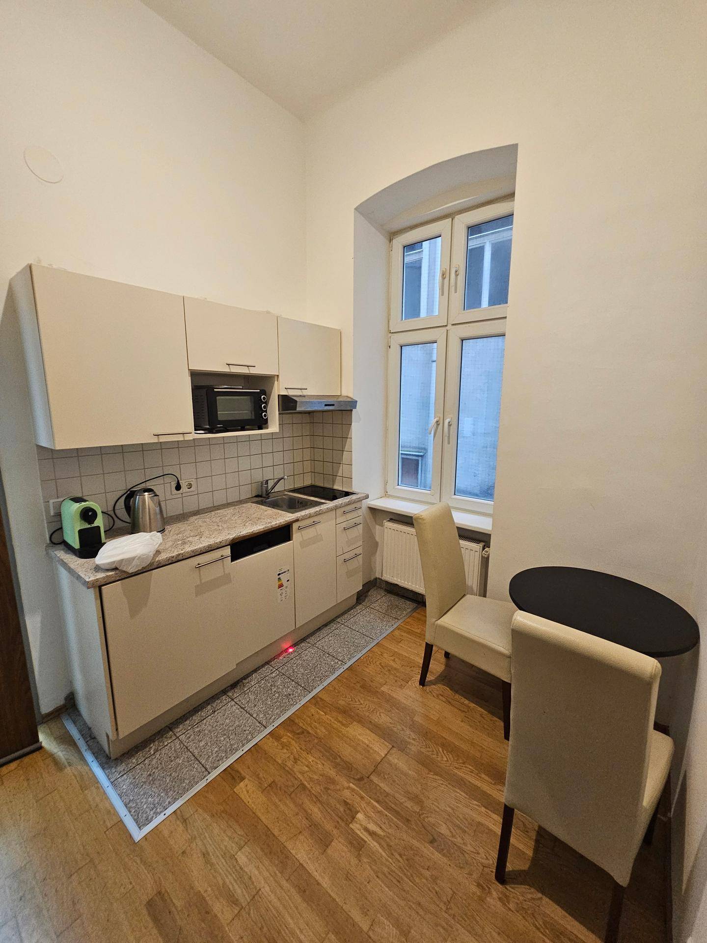 Kleine Küchenzeile mit Einbauschränken, Mikrowelle und Essbereich am Fenster.