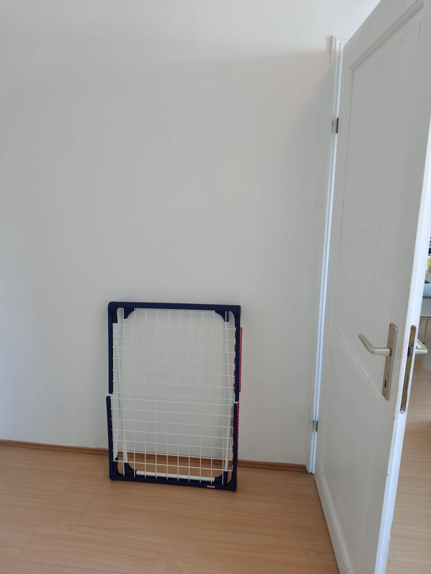 Leere Wand im Schlafzimmer mit Laminatboden und einem zusammengeklappten Wäscheständer.