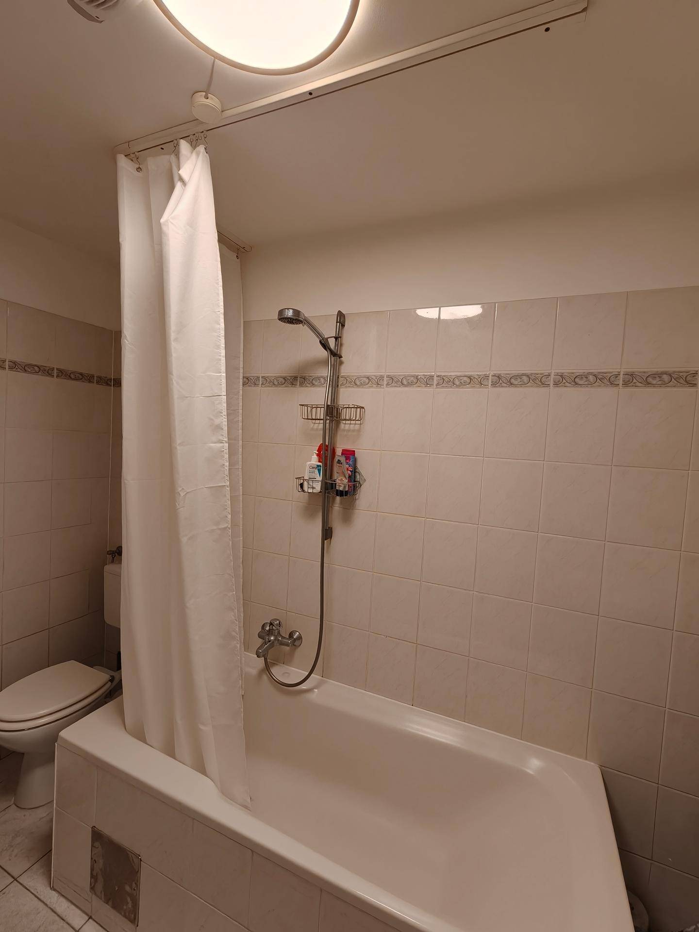 Badezimmer mit Badewanne, Duschkopf und hellen Fliesen an den Wänden.