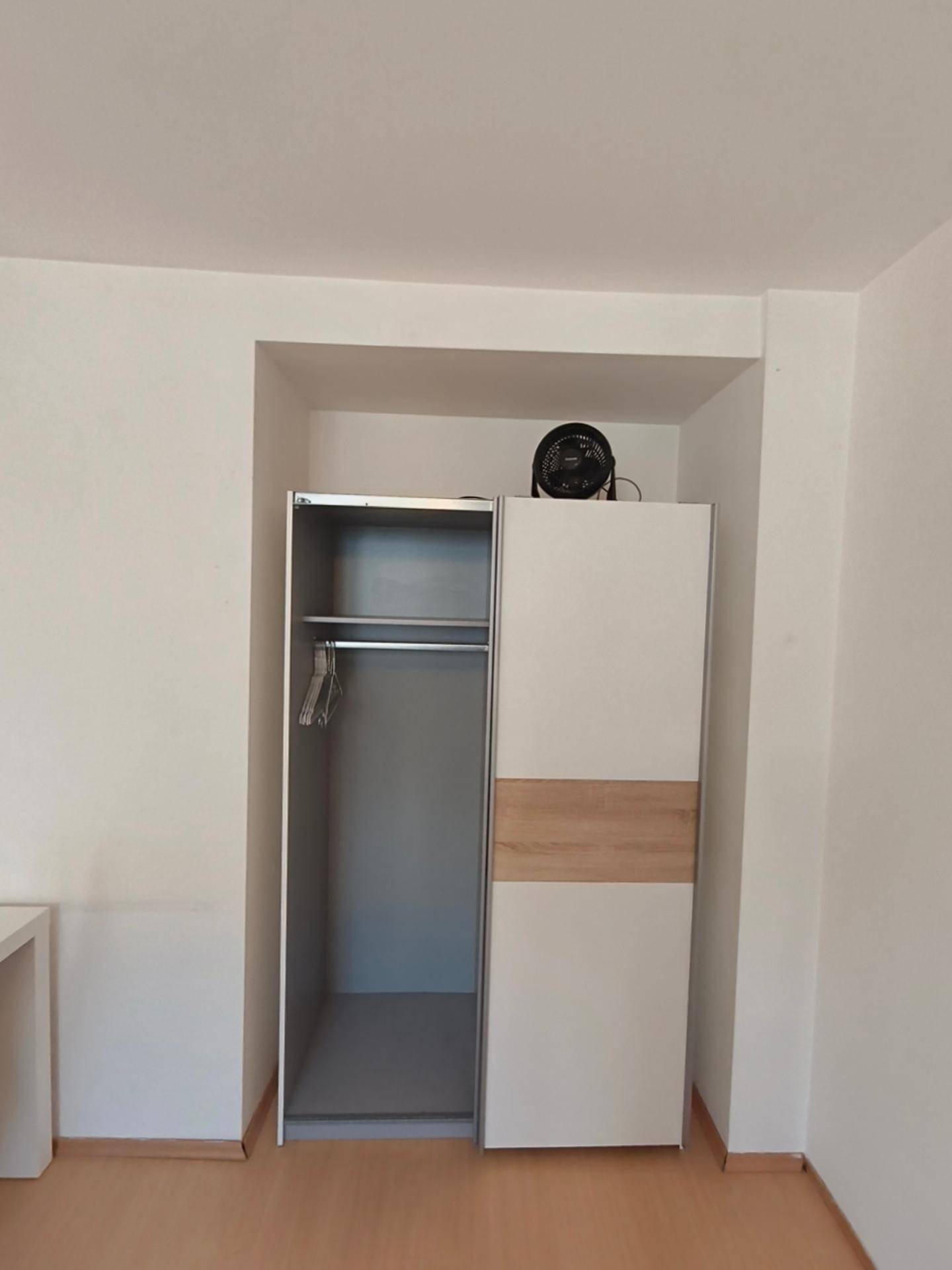 Offener Kleiderschrank in einer Nische mit Kleiderstange und Holzakzenten.
