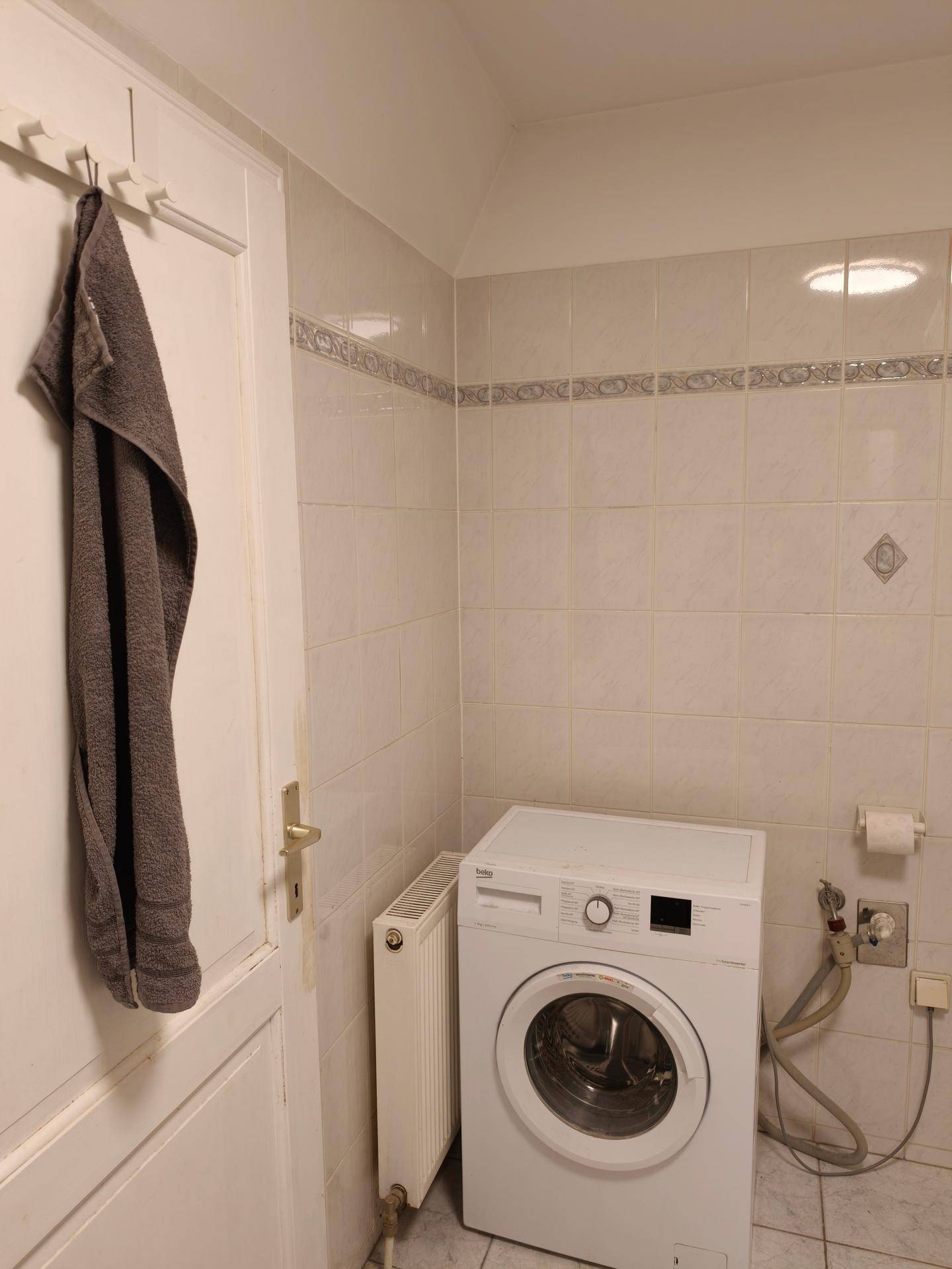 Badezimmer mit Waschmaschine, Heizkörper und hellen Fliesen an den Wänden.