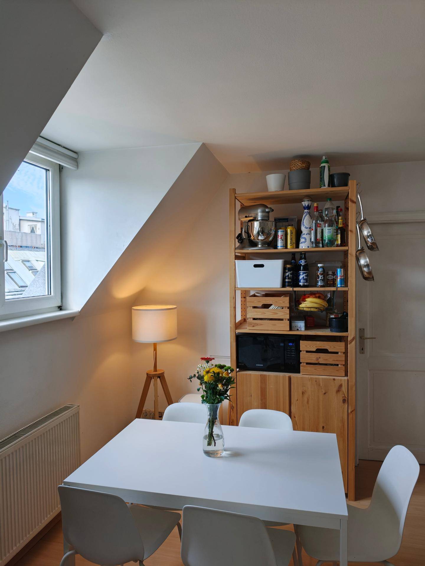 Heller Essbereich mit weißem Tisch, Stühlen und einem Holzregal in der Wohnküche.