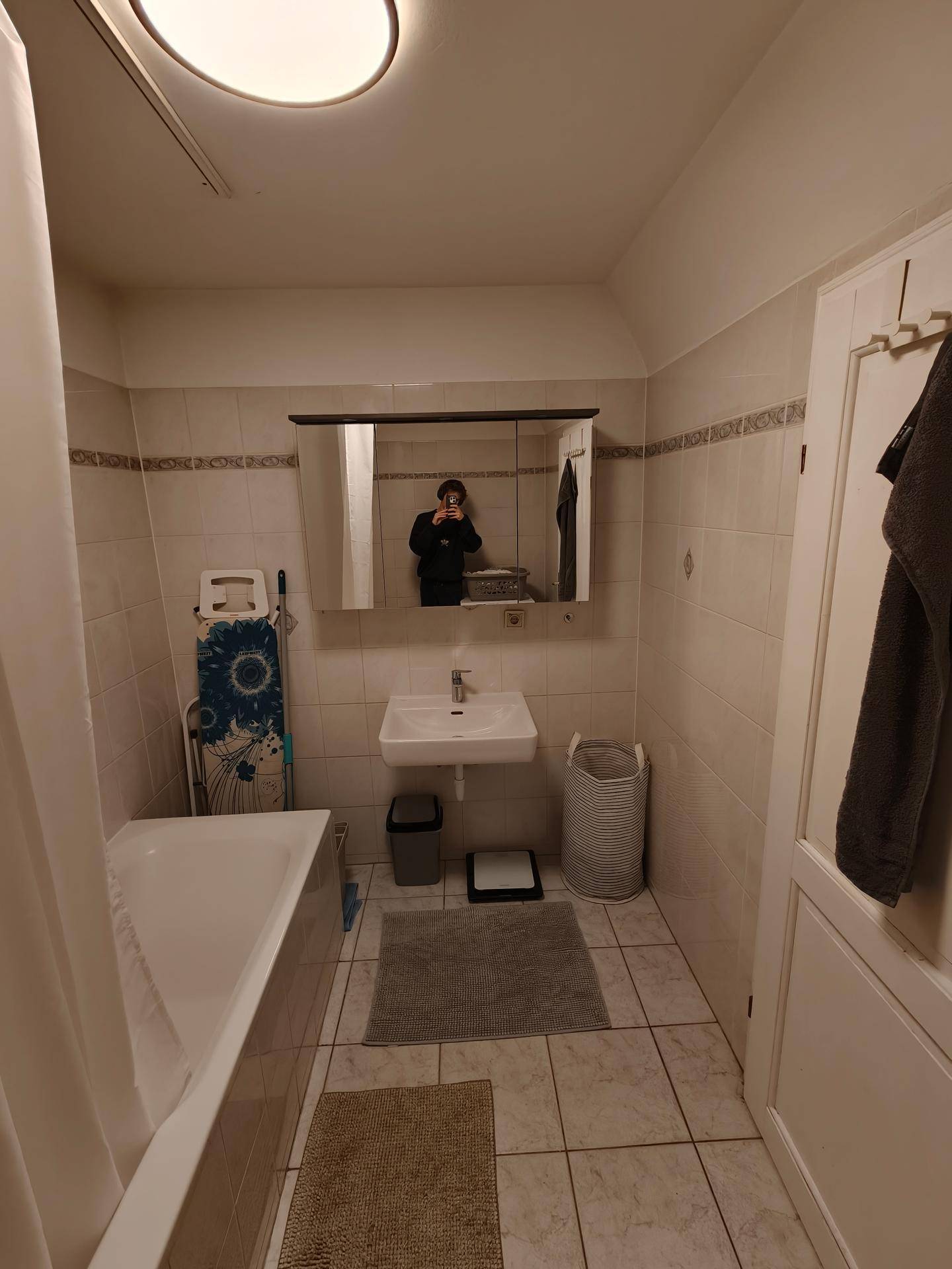 Gefliestes Badezimmer mit Badewanne, Waschbecken, Spiegelschrank und Handtuchheizkörper.