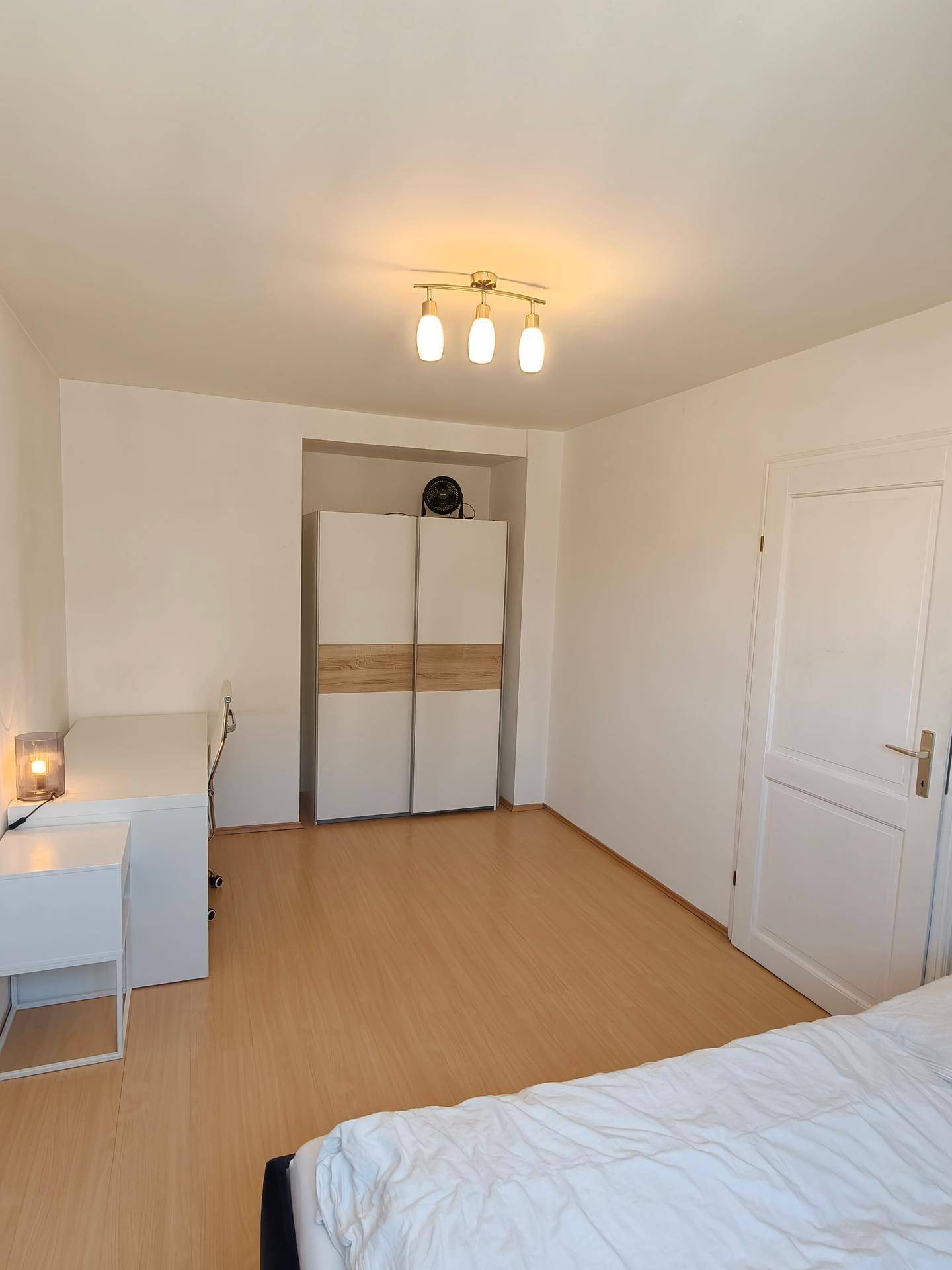 Schlafzimmer mit Laminatboden, einem Kleiderschrank in einer Nische und einem Schreibtisch.