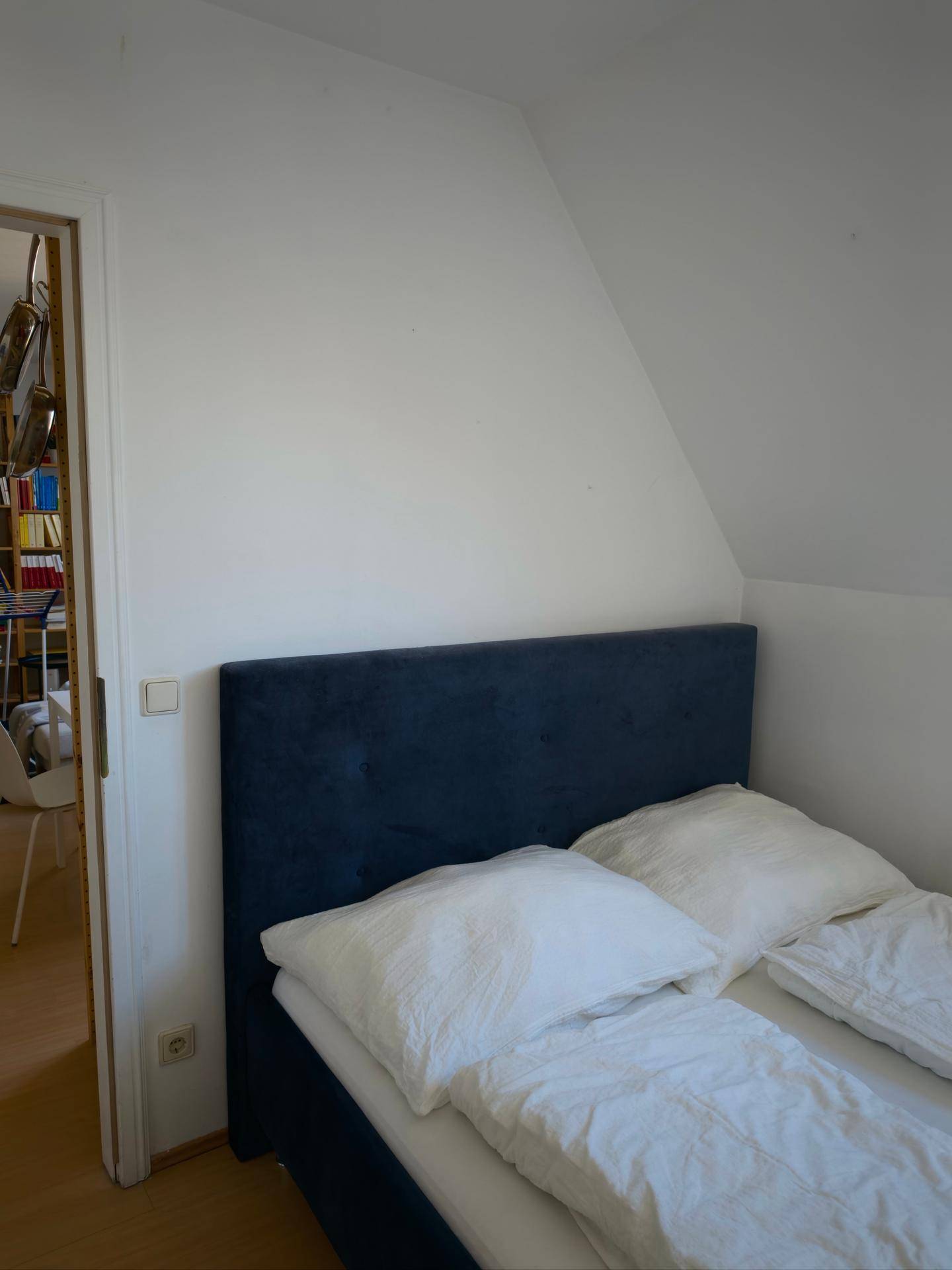 Nahaufnahme eines Bettes in einem Schlafzimmer mit Dachschräge und Zugang zu einem weiteren Raum.