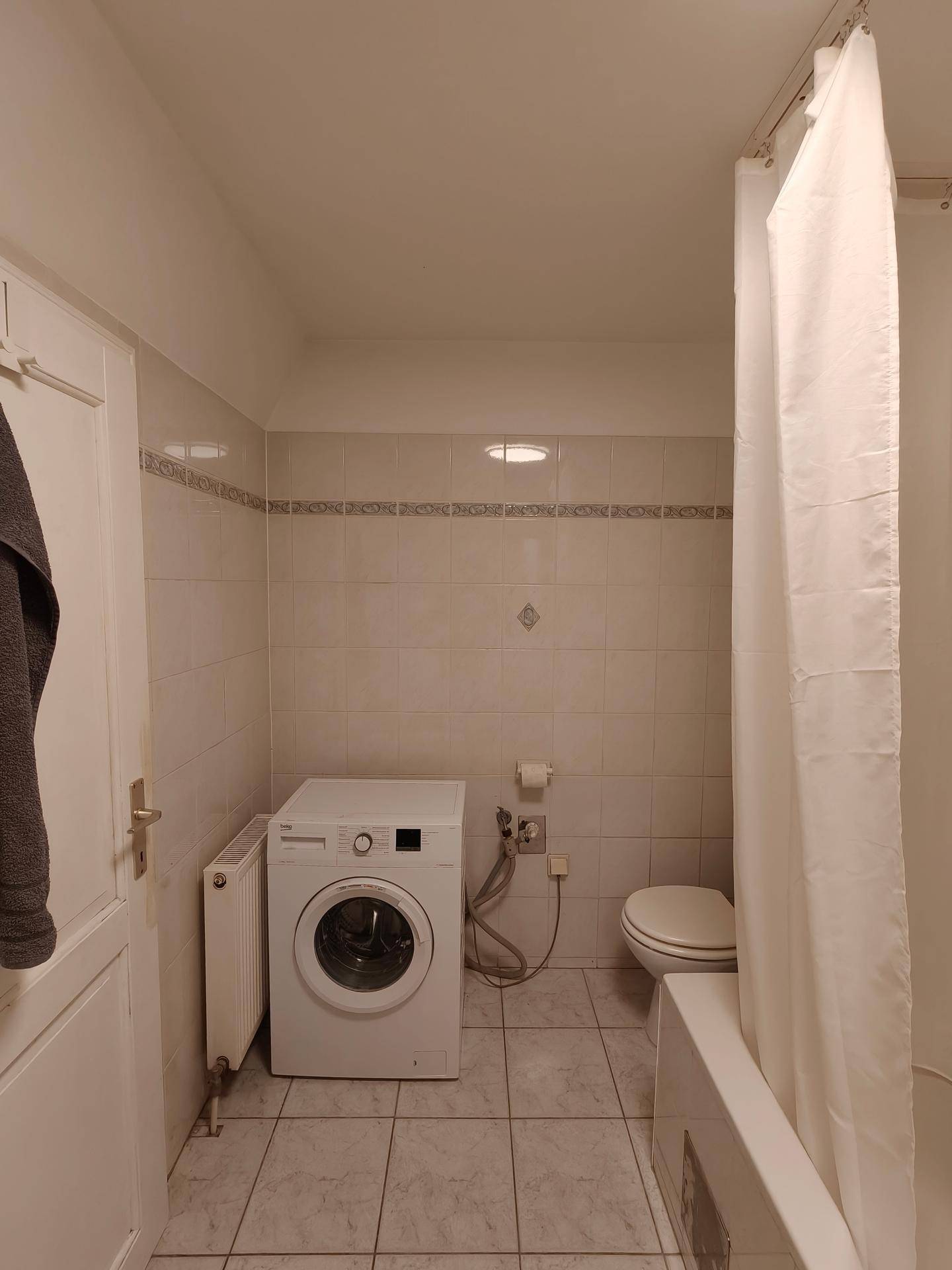 Badezimmer mit Waschmaschine, Toilette und Badewanne mit Duschvorhang.