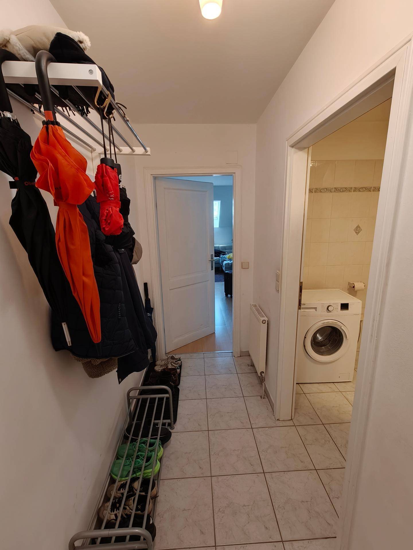Flur mit Garderobe und Schuhregal, der zum Badezimmer führt.