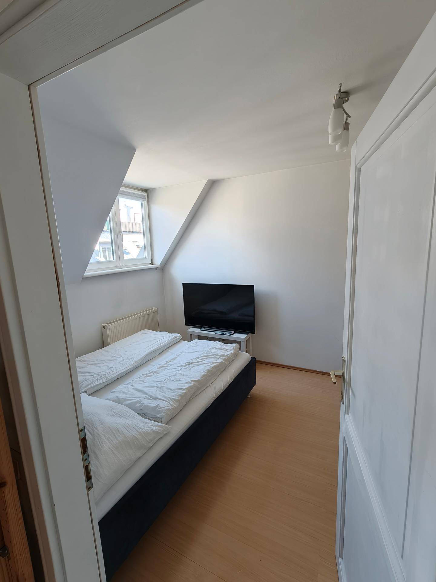 Blick durch die Tür in das Schlafzimmer mit Doppelbett, Fernseher und Dachschräge.
