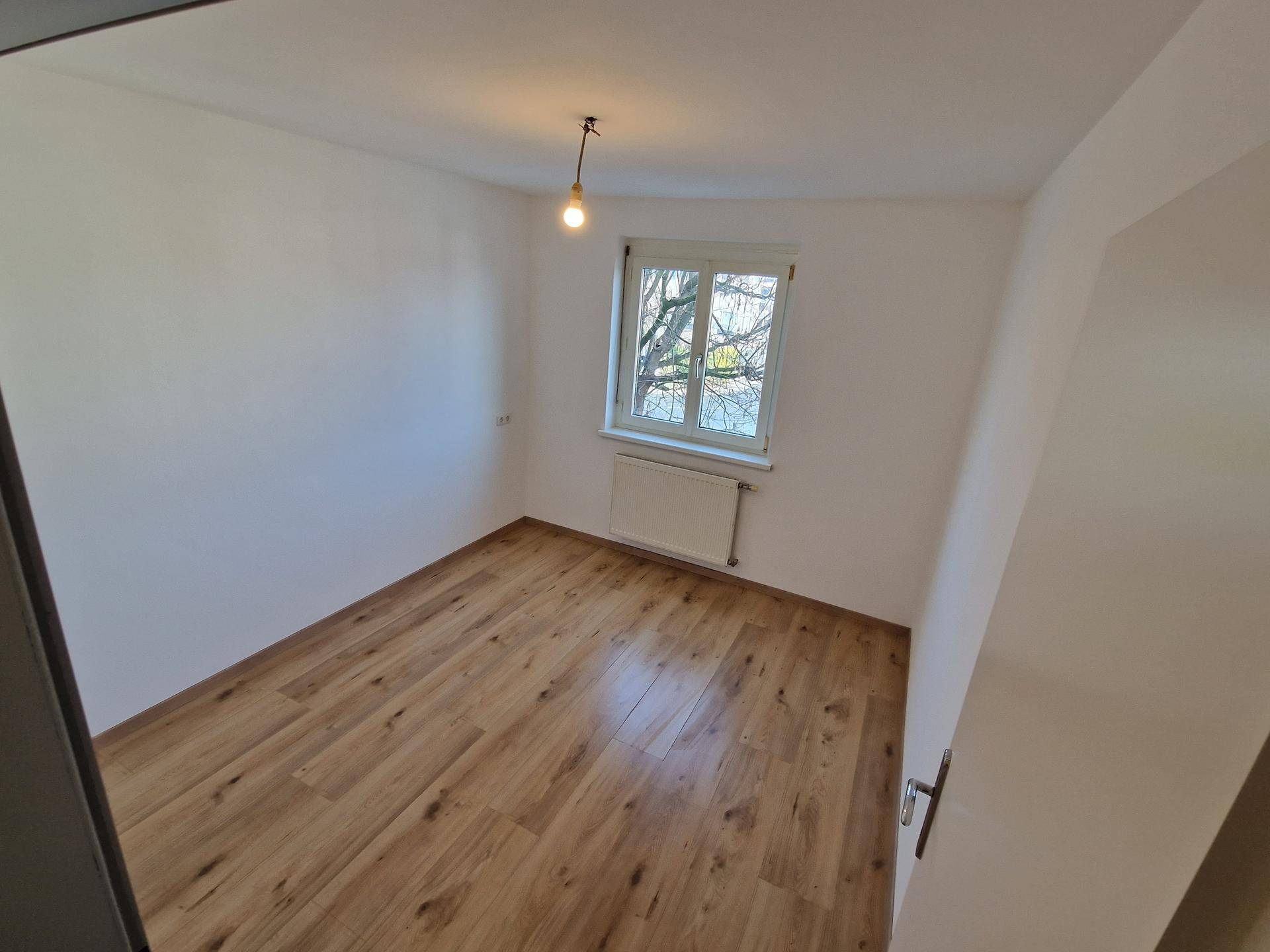 Helles Zimmer mit Laminatboden und einem Fenster, das viel natürliches Licht in den Raum bringt.