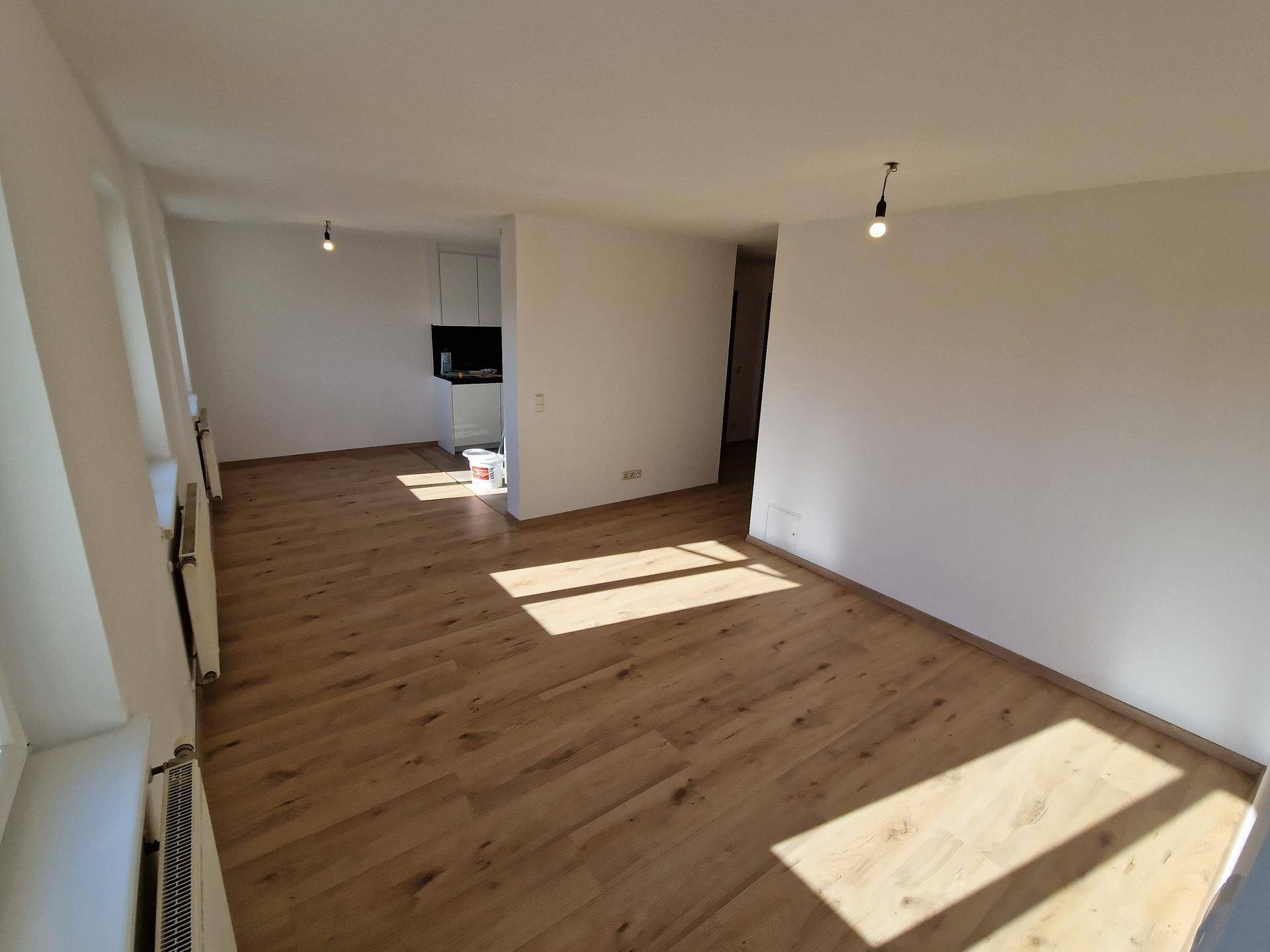 Heller, leerer Wohnbereich mit neuem Laminatboden und viel natürlichem Sonnenlicht.
