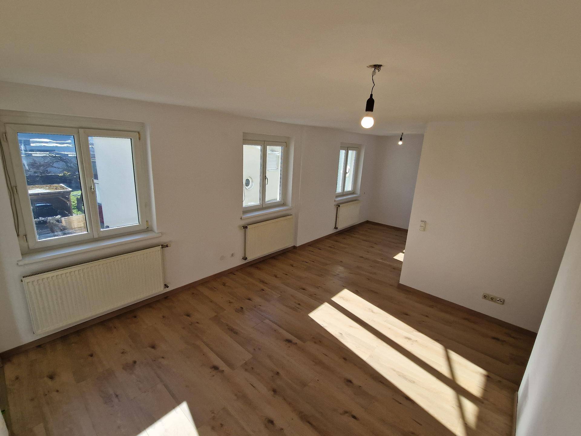Geräumiger Wohnbereich mit mehreren Fenstern, die viel Tageslicht hereinlassen, und Laminatboden.
