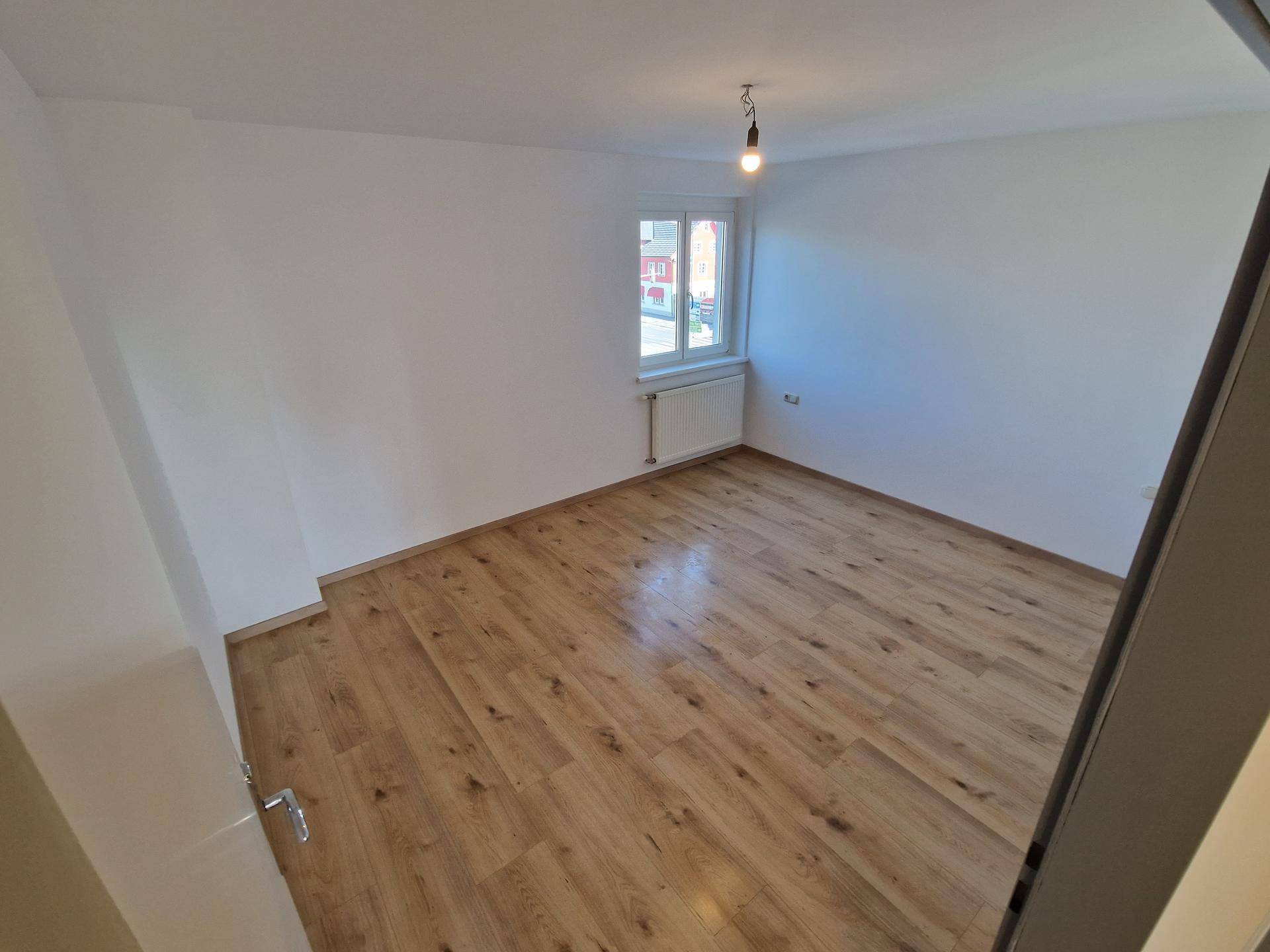 Leeres Schlafzimmer mit Laminatboden, weiß gestrichenen Wänden und einem Fenster für Tageslicht.