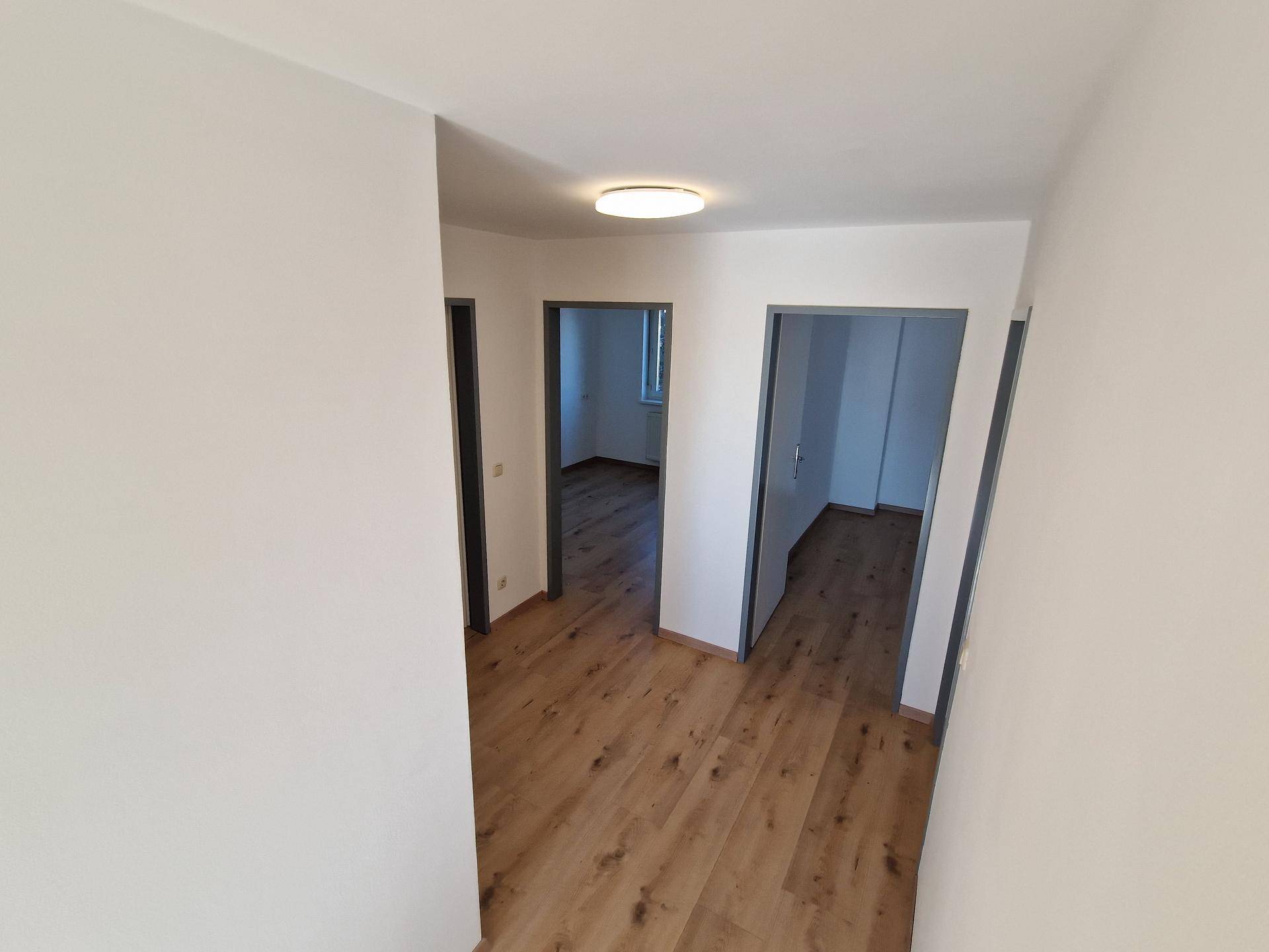 Heller Flur mit Laminatboden und Zugang zu mehreren Zimmern, frisch gestrichene Wände.