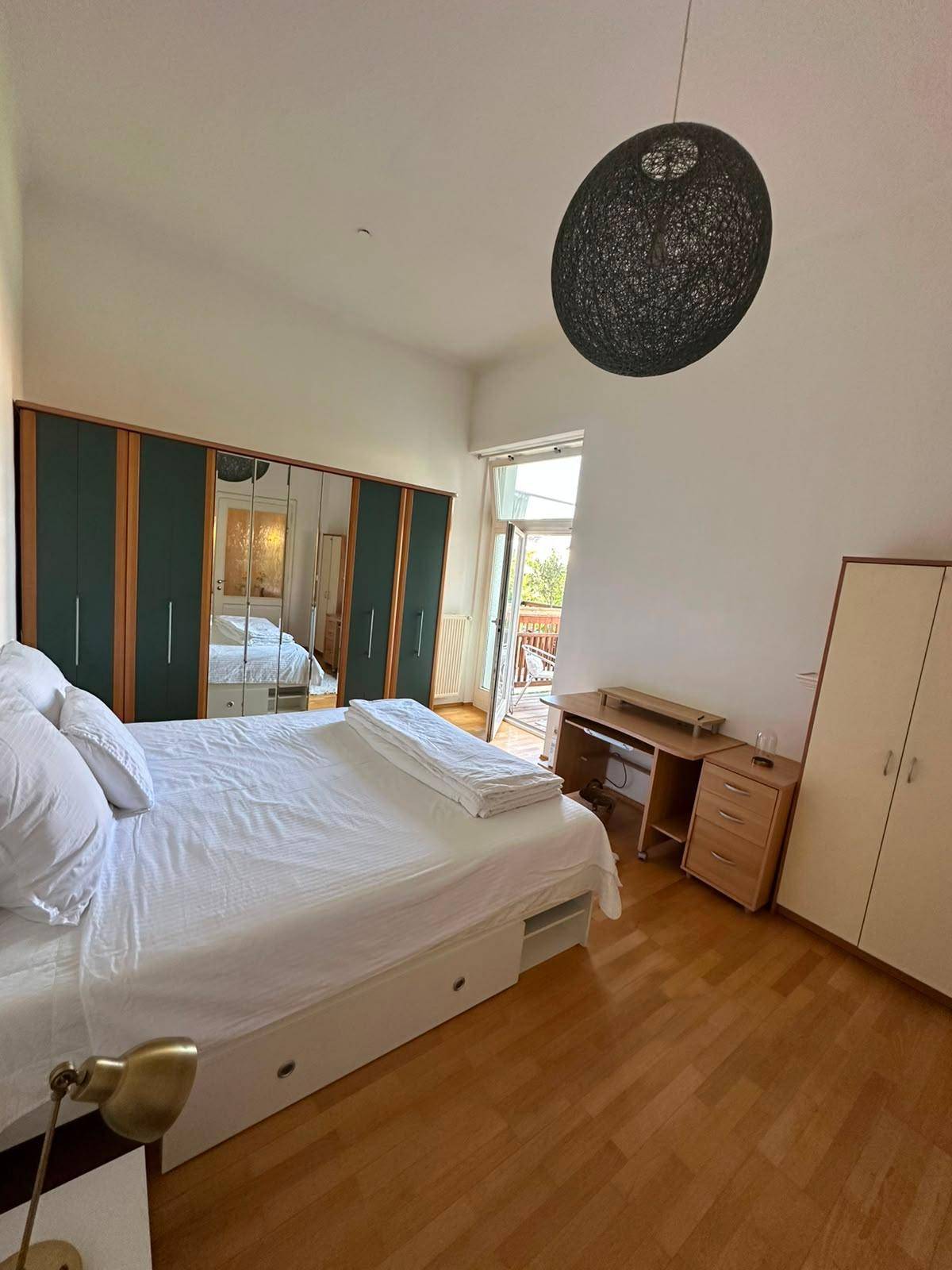 Helles Schlafzimmer mit Doppelbett, Kleiderschrank und Zugang zu einem Außenbereich.