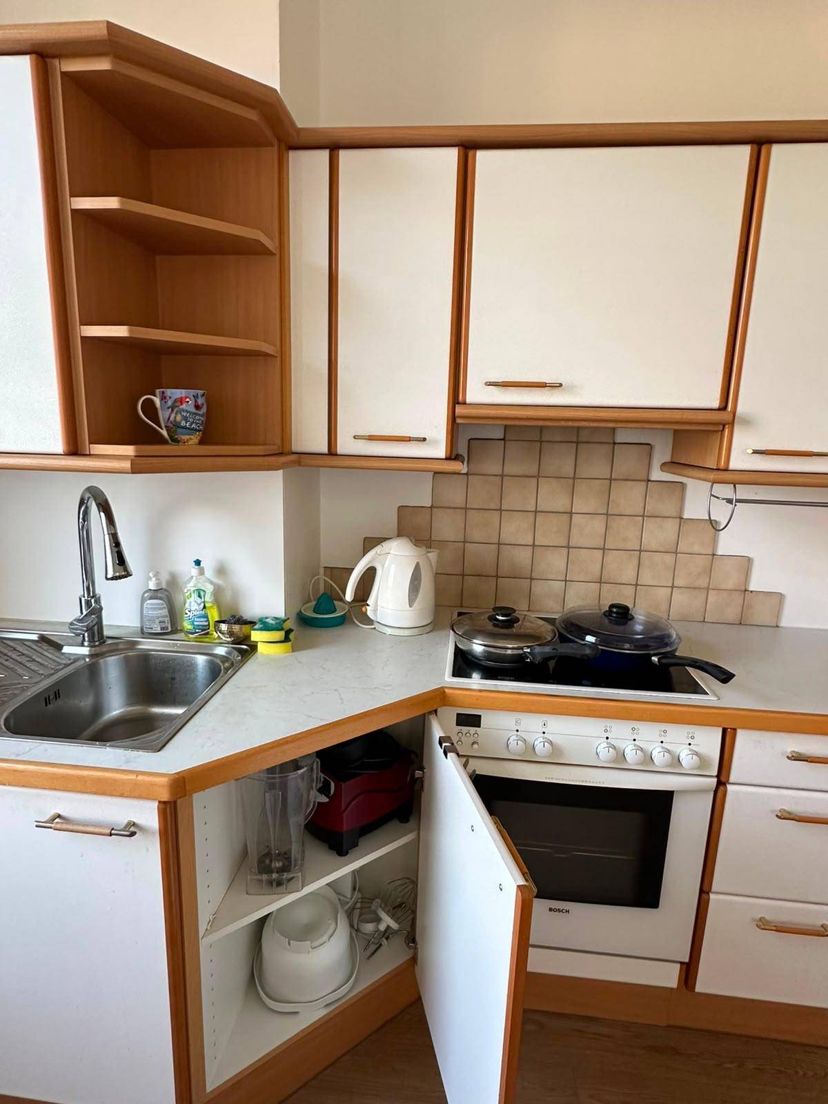 Detailansicht der Küche mit Spüle, Kochfeld, Backofen und hellen Holzschränken.